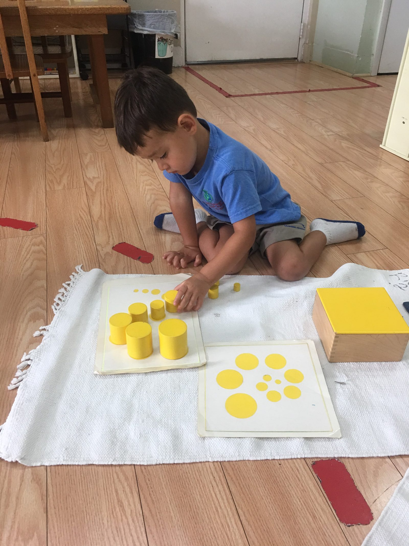 Boy working with Montessori knobbed cylinders on a mat