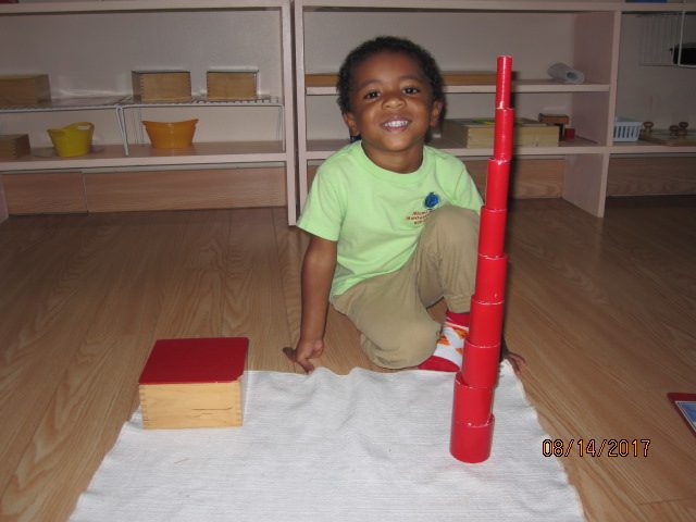 Young boy proudly building the Montessori pink tower