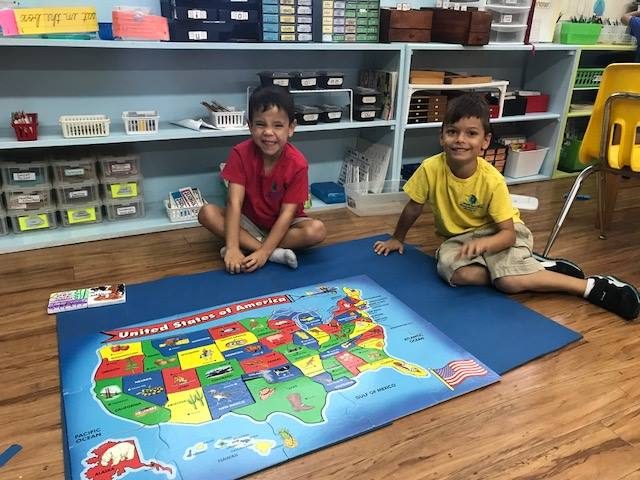 Two boys smiling behind a completed USA puzzle map